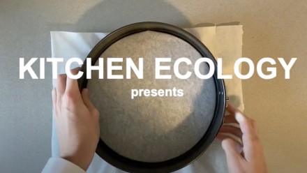 On a direct angle, the circular shape of a cake tin sits against a light grey kitchen counter. There is baking paper in the middle of the circle. Over the top of this symmetrical image are the words &#039;Kitchen Ecology&#039;