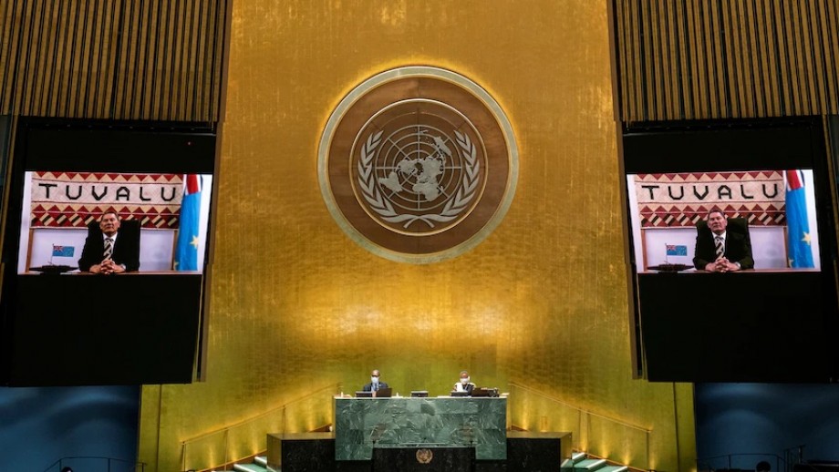 A photo of the Tuvaluan minister speaking to the UNHCR on two screens split across a large stage with the UNHCR laurel between them in gold.
