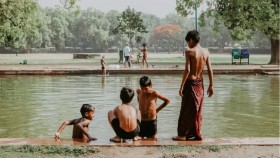 Four children sit on the edge of a water body in New Delhi, India.