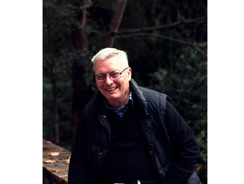 Dr Ian Fry is wearing glasses, a dark zippered vest and black top underneath, with a dark background. His hair is short and grey and he is smiling. Dr Ian Fry is wearing glasses, a dark zippered vest and black top underneath, with a dark background. His hair is short and grey and he is smiling.
