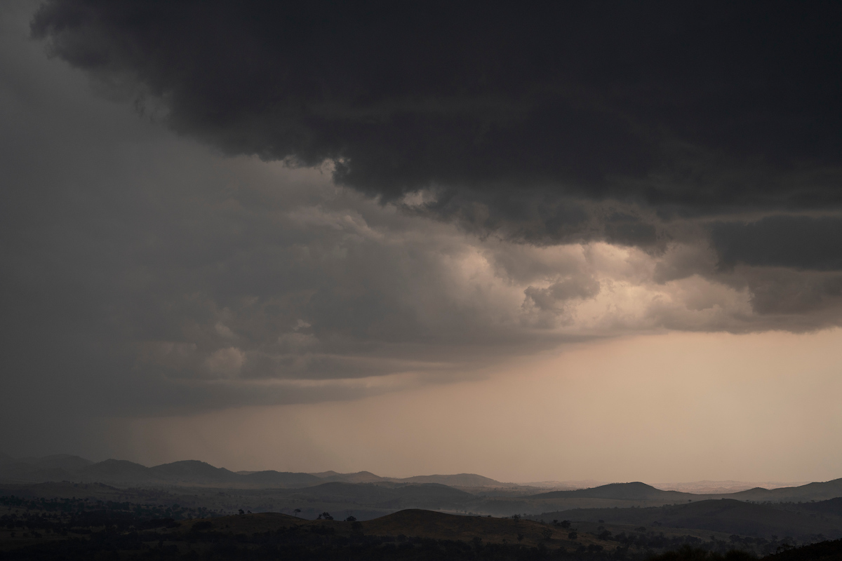 Storm cells move towards the ANU Mount Stromlo. Photo: Australian National University Dark storm clouds over a soft hilly landscape