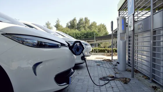 Electric cars are plugged in and charging at outdoor stations in a parking lot.