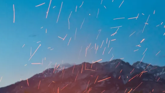 Orange streaks of light scatter across a twilight sky above silhouetted mountains.