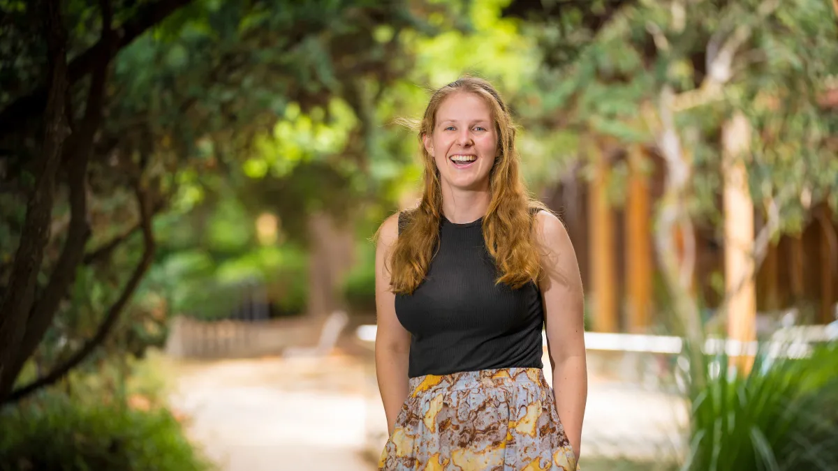 Isobel smiles and stands among greenery on campus.