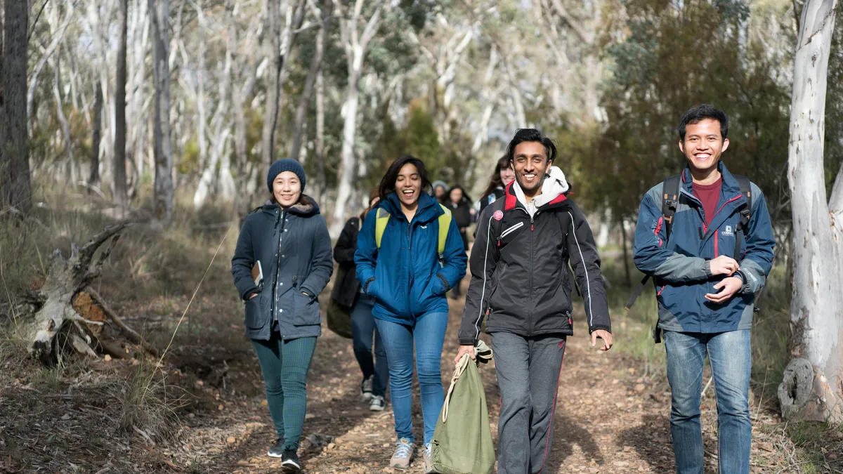 Students walk through the bush, smiling.