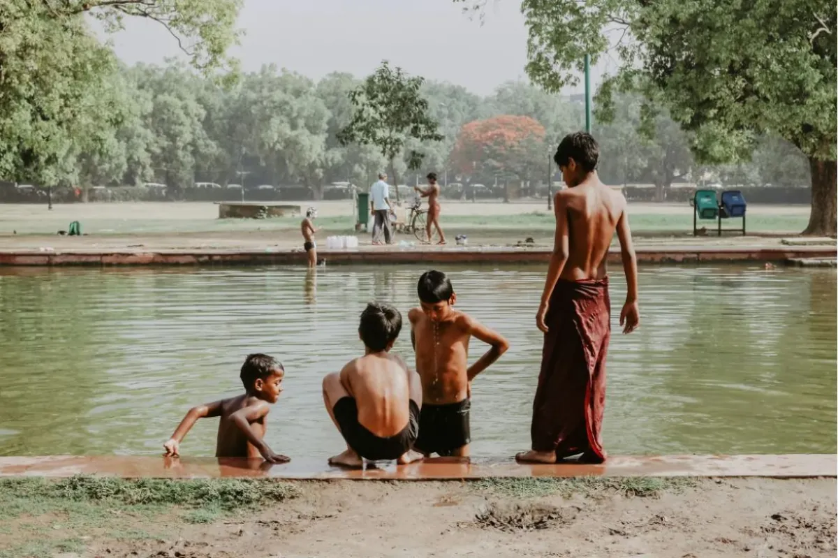 Four children sit on the edge of a water body in New Delhi, India.