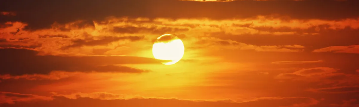 Sun shining through orange clouds at sunset.
