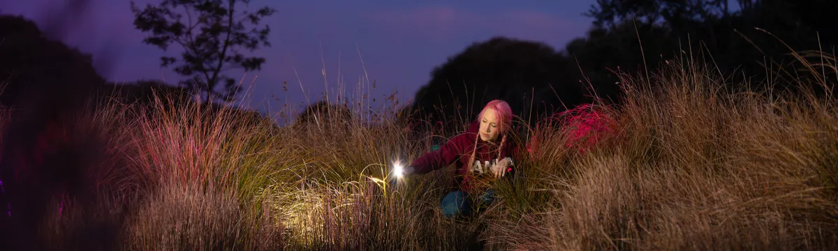 A researcher shines her spotlight into the edge of a dam at night.