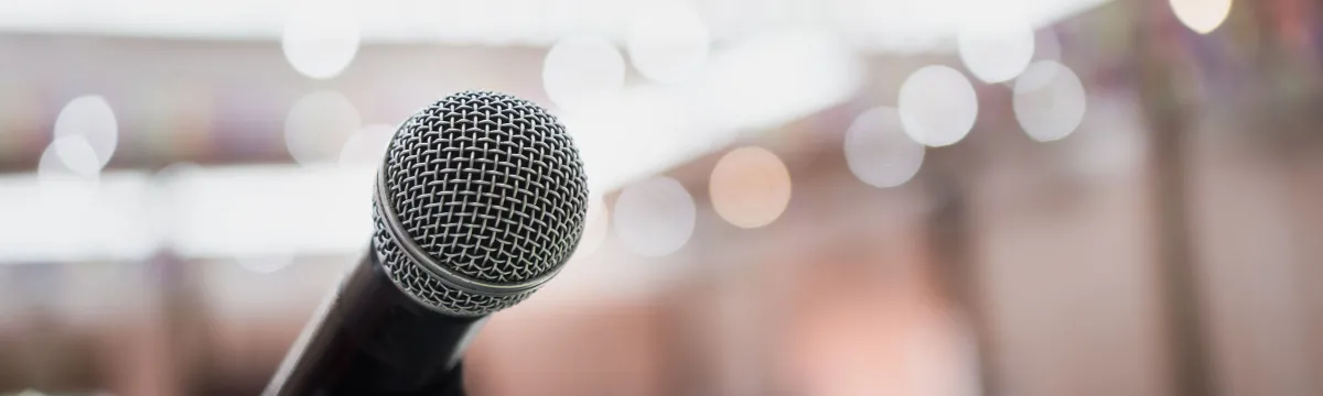 A silver microphone faces the viewer while the background is blurred, bright, with lots of lights.