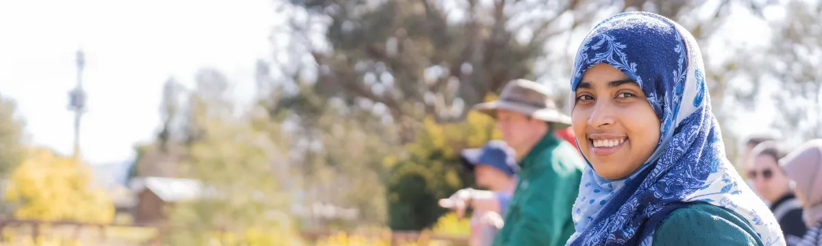 A student stands at the edge of a pond looking at the camera and holding onto a rail..