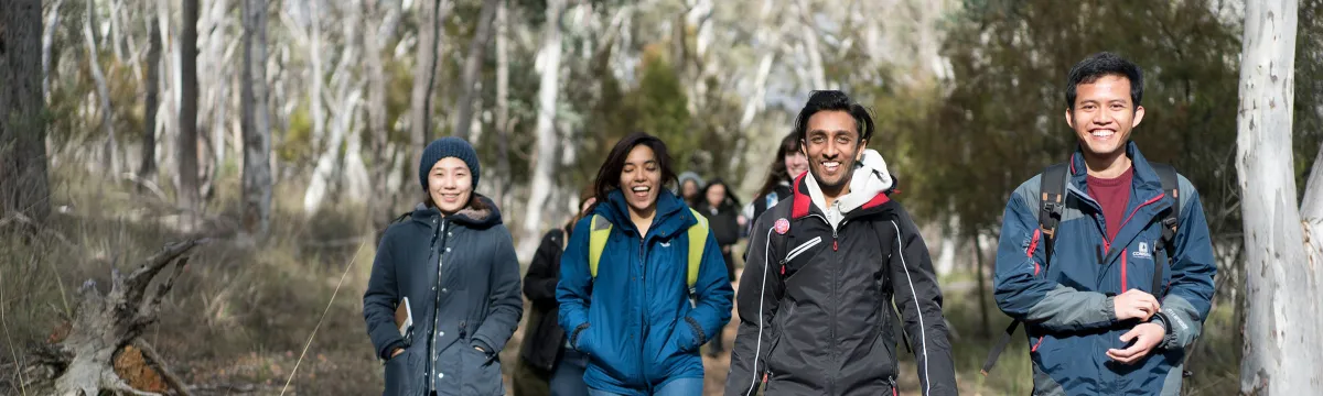 A group of students walk in the bush, smiling.
