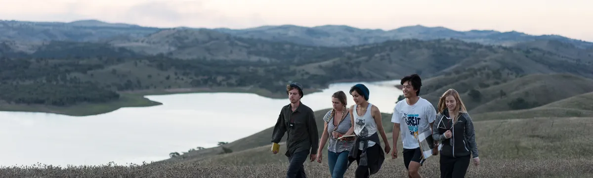 Group of students walking along a hill by a lake.