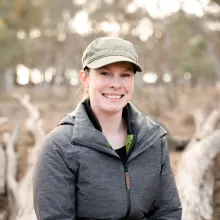 Belinda Wilson sits on a fallen tree in a woodland environment.