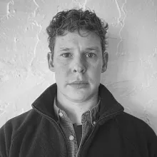 Portrait of PhD researcher, Sam Provost, facing the camera. Photo is in black and white.