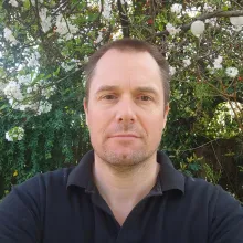 John Evans looks at the camera. He wears a black polo shirt.