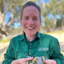 Giselle stands in a woodland environment holding superb parrot chicks.