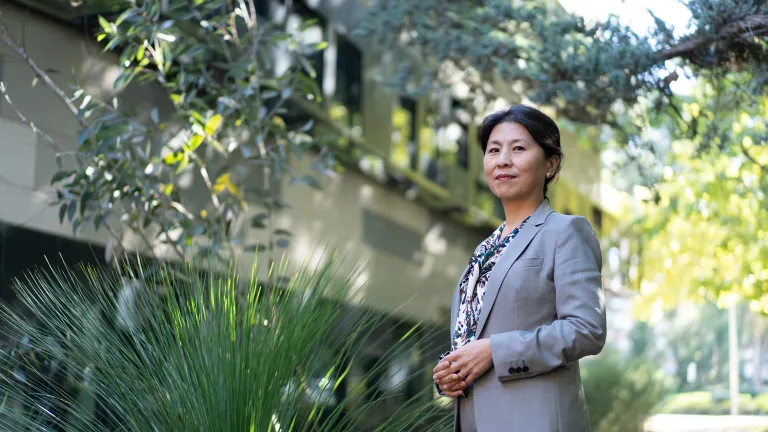 Researcher, Xuemei Bai, stands in front of the Fenner building with a grass tree beside her.