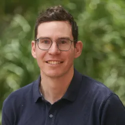 A portrait of Timothy Green. He wears glasses and a navy shirt.