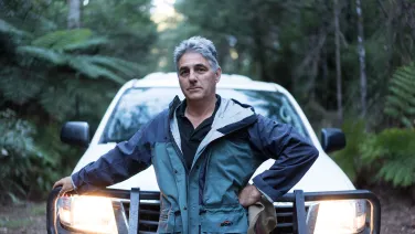 Professor David Lindenmayer stands in front of a car in the rainforest.