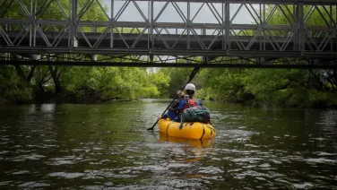 A researcher kayaks down a river in a yellow inflatable raft.