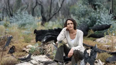 An academic, Marta Yebra, sits in front of a burnt landscape.