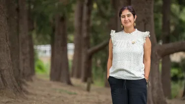 A woman in a white top standing in front of trees