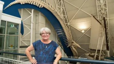 A professor stands in front of a skeleton of a whale.