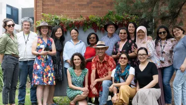 A group of students, staff and academics in colourful clothes pose together for a photo outside.