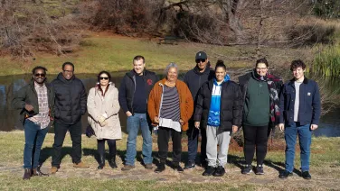 Researchers and collaborators stand in front of a pond at the ANU Campus.