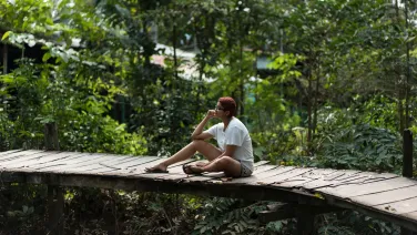 A student sits on a bridge in a tropical forest in Vietnam.