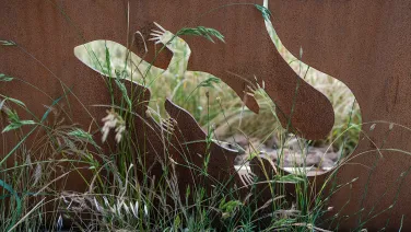 A corten steel cutout of a lizard among grass.