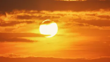 Sun shining through orange clouds at sunset.